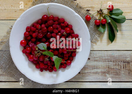 Reife süße Kirschen und Himbeeren in eine Schale auf einem Holztisch, Ansicht von oben. Platz für Ihren Text. Stockfoto
