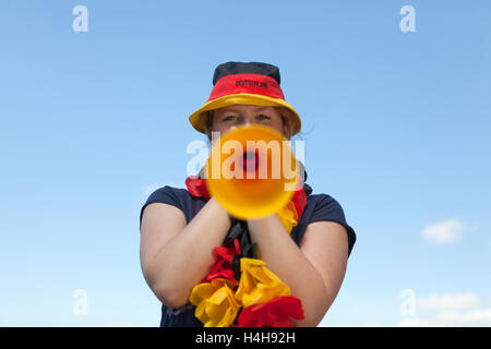 Junge Frau Blasen in einem Vuvuzela, schwarz rot gold, FIFA WM 2010 Stockfoto