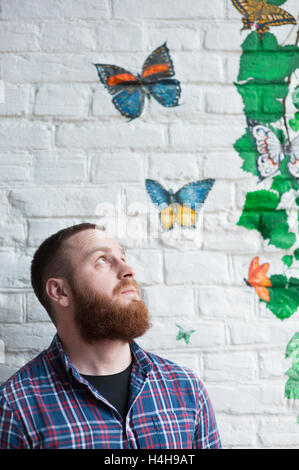 schöne bärtiger Mann schaut hinauf zum Graffiti mit Schmetterling Stockfoto