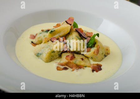 Spinat-Gnocchi mit Parmesan-Sauce, garniert mit Speck, reinigen dienen, Zutaten im Hintergrund Stockfoto