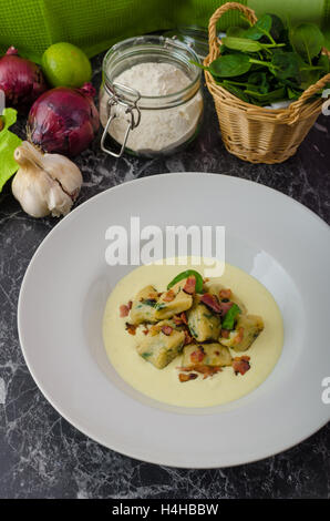 Spinat-Gnocchi mit Parmesan-Sauce, garniert mit Speck, reinigen dienen, Zutaten im Hintergrund Stockfoto