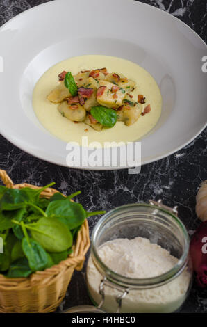 Spinat-Gnocchi mit Parmesan-Sauce, garniert mit Speck, reinigen dienen, Zutaten im Hintergrund Stockfoto