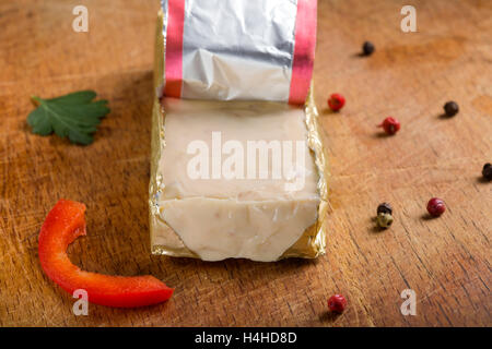 Block von Schmelzkäse in Goldfolie auf hölzernen Hintergrund Stockfoto