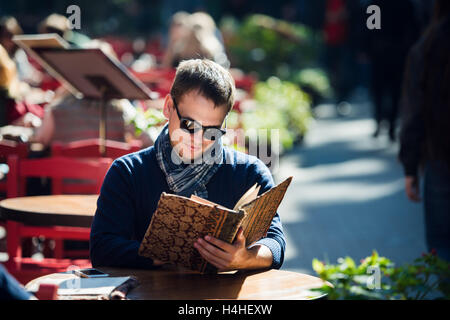 Hübscher junger Mann tragen Sonnenbrillen lesen die Morgenzeitung in einem Straßencafé Blick seitwärts. Kaffee-Pause. Stockfoto