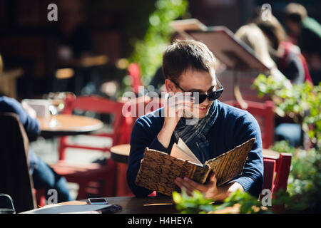 Cooler junger Mann in Sonnenbrille Bestellung etwas in einem Straßencafé Stockfoto