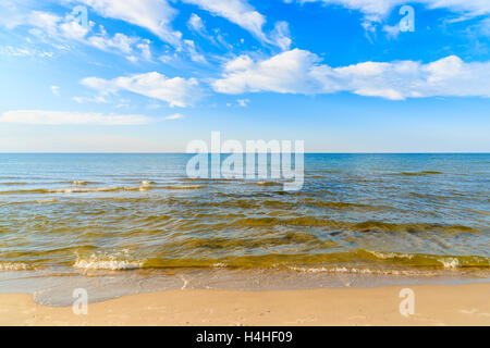 Wellen des Meeres auf Sandstrand und weißen sonnigen Wolken am blauen Himmel in Debki Dorf, Ostsee, Polen Stockfoto