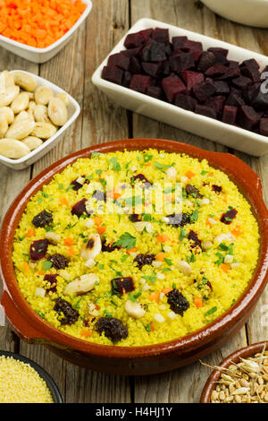 Vegetarisches Couscous in einem Tontopf mit Zutaten auf Schalen auf einem Holztisch Stockfoto