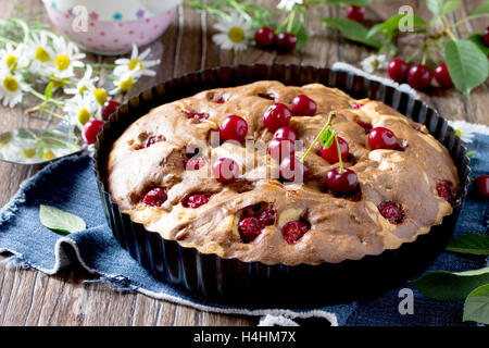 Hausgemachter Schokoladenkuchen mit Kirschen und frischen Beeren auf dem Holztisch. Stockfoto
