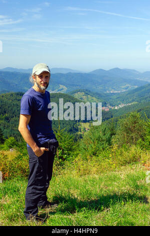 ein bärtiger Mann, Wanderer mit Rucksack, stehend in den Bergen und in die Ferne sieht. Hinten Sie Ansicht von. Sonniger Tag. Stockfoto