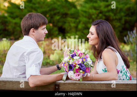 Liebespaar sitzen auf Bank mit Blumenstrauß Stockfoto