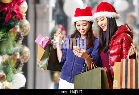 zwei jungen, asiatischen Frauen Blick auf Handy beim Weihnachts-shopping Stockfoto