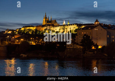 Prager Burg (Pražský Hrad) als Abenddämmerung und die Scheinwerfer und Straßenlaternen eingeschaltet sind. Reflexionen in der Moldau Stockfoto