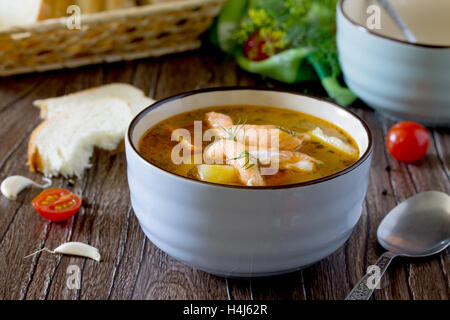 Tomatensuppe mit roter Fisch in einer Keramikschale auf einer Serviette, Tomaten, Petersilie, Brot auf Holzbrettern Hintergrund. Stockfoto