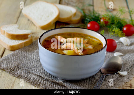 Tomatensuppe mit Lachs in einer Keramikschale, Brot und Tomaten auf einem hölzernen Brettern Hintergrund. Stockfoto