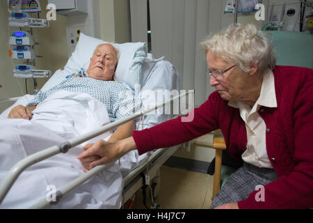 Ältere Menschen (83) erholt sich in seinem Krankenhausbett mit seine Frau neben ihm nach einer schweren Operation, UK Stockfoto