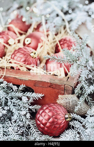 Glas Christbaumschmuck verpackt in einer alten antiken Holzkiste mit Schnee bedeckten Kiefer Ästen um sie herum. Stockfoto