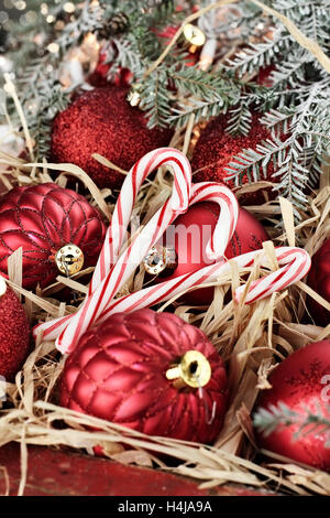 Drei Zuckerstangen und Weihnachtsschmuck verpackt in einer alten antiken Holzkiste mit Schnee bedeckten Kiefer Ästen um sie herum. Stockfoto