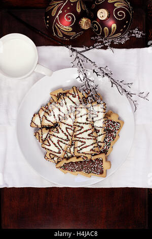 Teller mit Weihnachtsbaum geformt Cookies mit Tasse Milch und schöne Ornamente im Hintergrund. Stockfoto