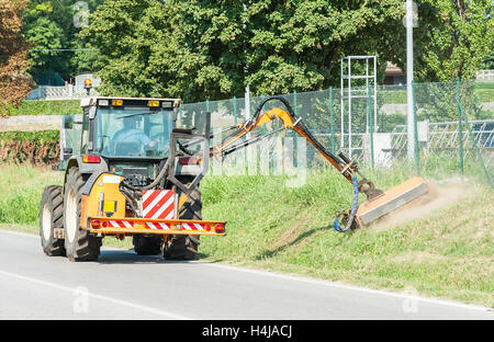 Straßenmeisterei. Rasenmähen am Straßenrand mit Traktor. Stockfoto