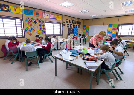Junior Schülerinnen und Schüler mit Lehrerin konzentrieren sich auf ihr Studium an ihren Schreibtischen in modernen luftig leichte Schulklasse Stockfoto