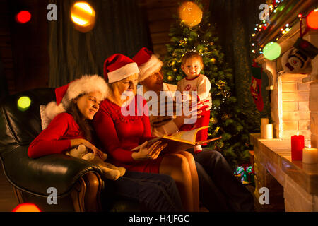 Familie - Papa, Mama mit Töchtern auf Sofa sitzen und lesen in der Nähe von Kamin Stockfoto