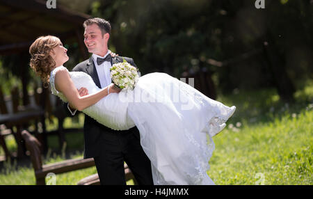 Bräutigam trägt Braut im Freien und lächelnd Stockfoto