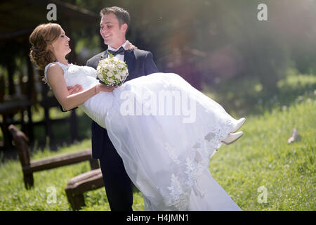 Bräutigam trägt Braut im Freien und lächelnd Stockfoto