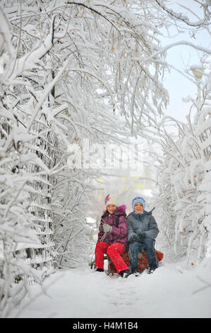 Zwei Kinder schieben mit Rodeln im Schnee Stockfoto