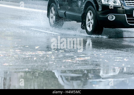 Auto fahren durch Wasser Pfütze und reflektieren es. Stadt-Straße nach herbstlichen Regen. Stockfoto