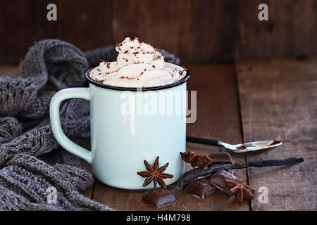 Emaille Tasse heißen Kakao oder Kaffee zu Weihnachten mit Schlagsahne, rasierte Schokolade, Vanilleschote, Gewürze und grauen Schal. Stockfoto