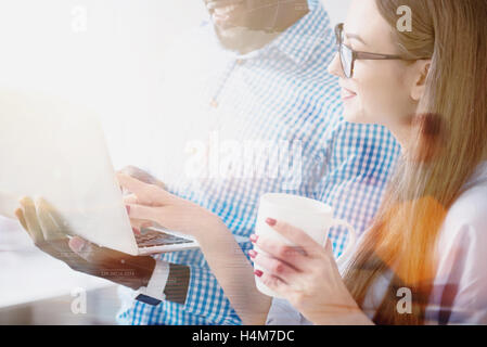 Junge hübsche Frau zeigt auf Laptop ihres Kollegen Stockfoto