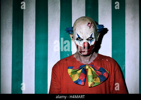 Nahaufnahme eines unheimlich böse Clown in einem schmutzigen Kostüm, mit dem Zirkuszelt im Hintergrund Stockfoto