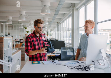 Aufnahme von zwei jungen Entwicklern testen virtual-Reality Brille im Amt. Kollegen arbeiten in modernen Büros, steht ein Stockfoto