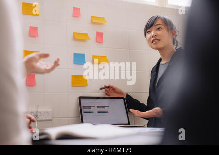 Asiatische Geschäftsfrau präsentieren ihre neuen Ideen auf den Laptop und Klebstoff Notizen an Wand. Junge weibliche Führungskraft, Vortrag Stockfoto