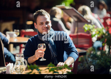 Junger Mann sitzt am Tisch outdoor-Bar mit einem Glas Weißwein ablöschen und auf die Kamera Stockfoto