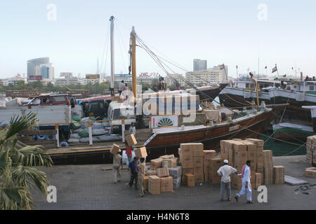 Boxen werden manuell auf einem traditionellen Holz Frachtschiff vor Anker in The Creek in Dubai geladen. Im Hintergrund die Skyline der Stadt Stockfoto