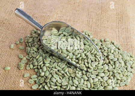 Grüne Kaffeebohnen in Metall Schaufel auf Sackleinen Oberfläche Stockfoto