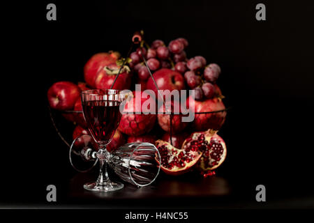 Still-Leben auf einem dunklen Hintergrund. Weingläser (Liquor), Früchte und Beeren (Äpfel, Granatäpfel und Trauben) in den Korb. Stockfoto