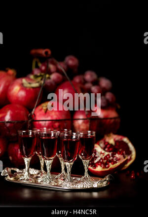 Still-Leben auf einem dunklen Hintergrund. Weingläser (Liquor), Früchte und Beeren (Äpfel, Granatäpfel und Trauben) in den Korb. Stockfoto