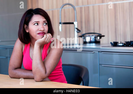 Porträt von hispanic Frau in der Küche sitzen und schauen gelangweilt Stockfoto