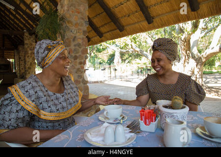 Porträt von zwei afrikanischen Frauen in traditionellen Seshweshwe Kleid teilen einen Witz beim Sitzen am ein Außenrestaurant mit Kaffee Stockfoto