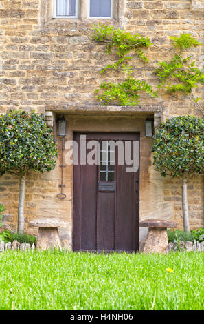 Braune hölzerne Außentüren des traditionellen englischen Cottage mit Formschnitt Lorbeer Bäume, Staddle Steinen, Rasen Rasen vor Stockfoto