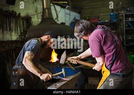 Zwei Schmiede hammer ein Stück Metall auf Amboss in einer Werkstatt Stockfoto