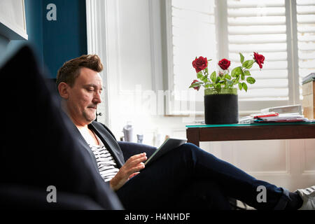 Mann im Büro mit seinem Mobiltelefon, eine Vase mit roten Rosen auf einem Schreibtisch sitzt. Stockfoto