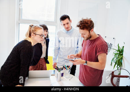 Vier Personen um einen Tisch bei einem Geschäftstreffen, einem digitalen Tablet-Bildschirm betrachten. Stockfoto