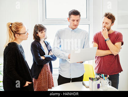 Vier Personen an einem Tisch auf einem Business-Meeting, einem Laptop-Bildschirm betrachten. Stockfoto