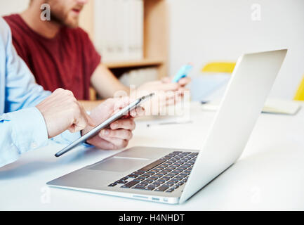 Zwei Männer mit einem Laptop-Computer, mit einem digitalen Tablet und Blick auf ein smart Phone. Stockfoto