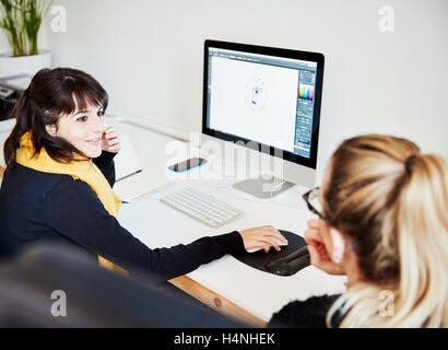 Zwei Frauen sitzen einen Computer-Bildschirm teilen und diskutieren die grafischen Inhalten. Stockfoto