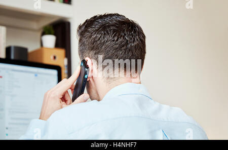 Ein Mann einen Anruf tätigen und mit Blick auf seinem Computerbildschirm. Stockfoto