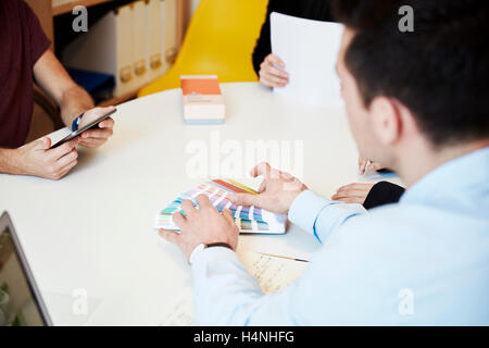 Drei Personen rund um einen Tisch, mit einem Tablet, zeigt eine Farbkarte. Designer. Stockfoto